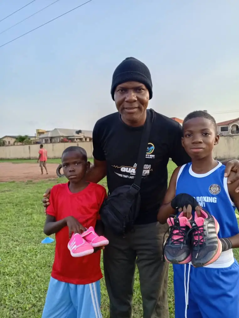 A coach with two young boxers, each holding a new pair of training shoes