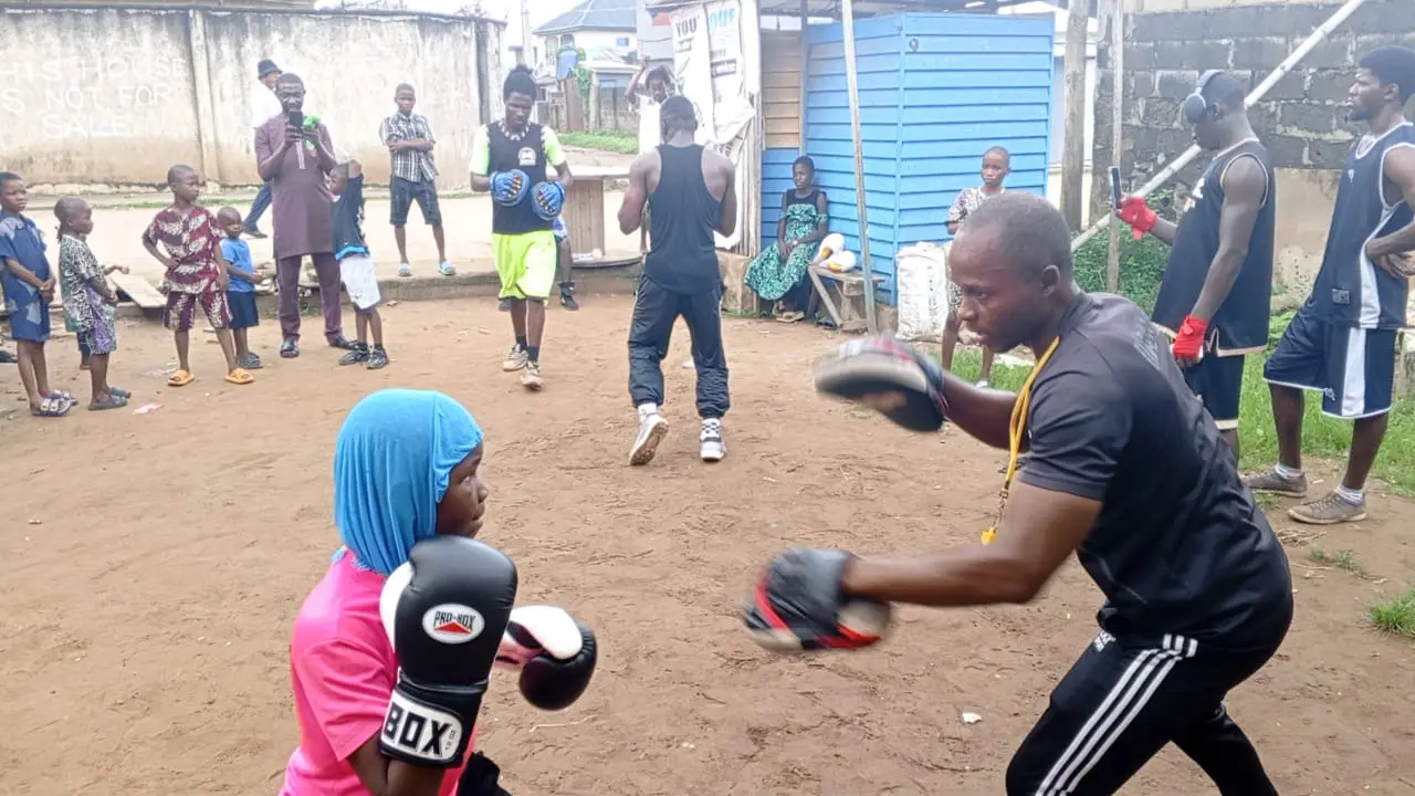 A girl in a pink top punching pads held by a coach