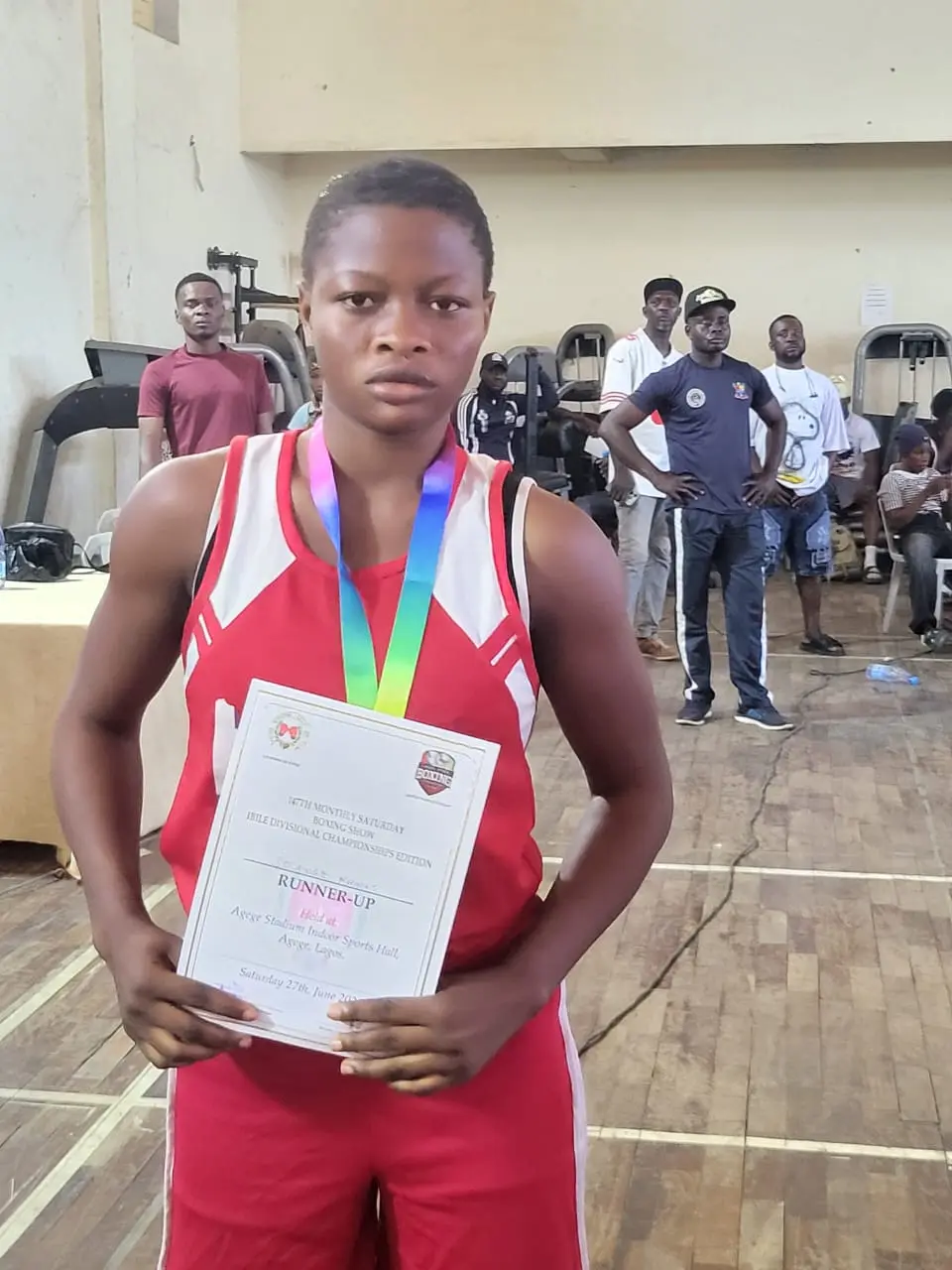 A young boxer in a red vest wearing her medal and holding her certificate